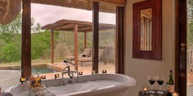 Freestanding bathtub with bush and pool views, candles and wine at Kwandwe Great Fish River Lodge, Eastern Cape, South Africa