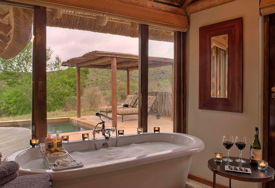 Freestanding bathtub with bush and pool views, candles and wine at Kwandwe Great Fish River Lodge, Eastern Cape, South Africa