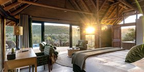 Luxury thatched bedroom with king bed and golden sunrise light flooding through glass doors at Kwandwe Great Fish River Lodge