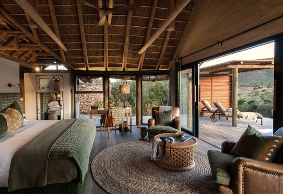 Luxury thatched bedroom suite with king bed, leather armchairs and private deck with bush views at Kwandwe Great Fish River Lodge, Eastern Cape