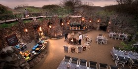 Dramatic torchlit boma dinner setting with stone walls and central fire at andBeyond Phinda Mountain Lodge, KwaZulu-Natal