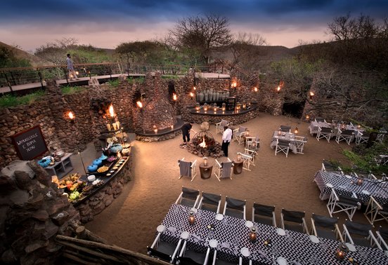 Dramatic torchlit boma dinner setting with stone walls and central fire at andBeyond Phinda Mountain Lodge, KwaZulu-Natal