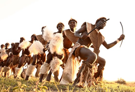 Zulu dancers in traditional dress performing at golden hour in Phinda Private Game Reserve, KwaZulu-Natal, South Africa