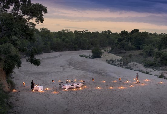 Candlelit dinner table set in a dry riverbed at dusk in Timbavati, South Africa