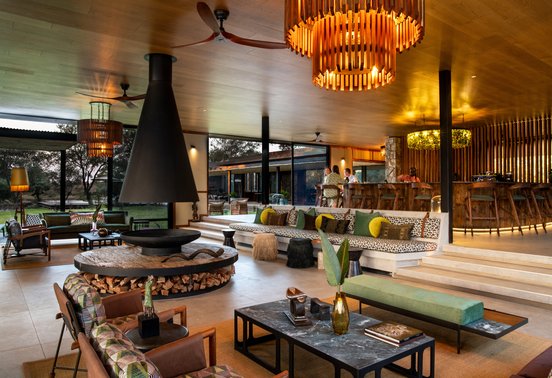 Stylish open-plan lounge and bar area with fireplace and designer lighting at Tanda Tula Safari Camp, Timbavati