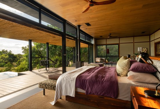 Luxury suite bedroom with floor-to-ceiling glass walls overlooking the Timbavati bush at Tanda Tula Safari Camp