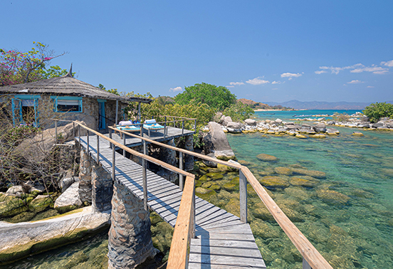 Stone chalet perched above turquoise waters connected by wooden walkway at Kaya Mawa, Likoma Island.