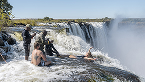 Travelers experience Devil’s Pool on the edge of Victoria Falls, with guides present as water flows over the drop.