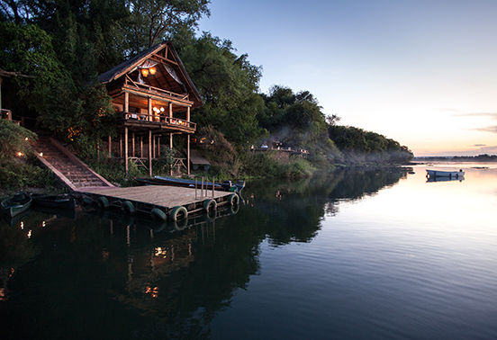 Riverfront house at Tongabezi Lodge overlooking the Zambezi River at sunset, with a private jetty below.