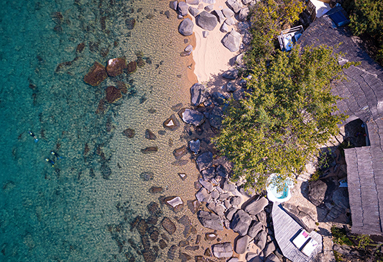 Aerial view of Kaya Mawa’s lakeside setting on Likoma Island, with clear shallows, beach, and stone chalets.