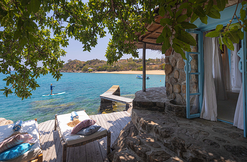 Stone villa at Kaya Mawa overlooking Lake Malawi with paddleboarder on turquoise water.