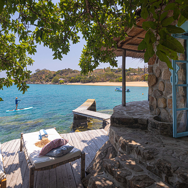 Stone villa at Kaya Mawa overlooking Lake Malawi with paddleboarder on turquoise water.