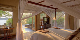 Riverfront suite at Ila Safari Lodge with canopy bed and open doors overlooking the Kafue River.