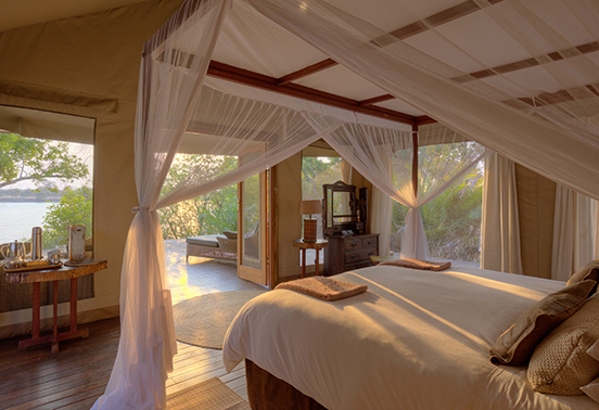 Riverfront suite at Ila Safari Lodge with canopy bed and open doors overlooking the Kafue River.