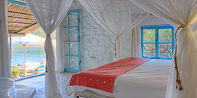 Light-filled bedroom with canopy bed, whitewashed stone walls, and lake views at Kaya Mawa, Likoma Island.