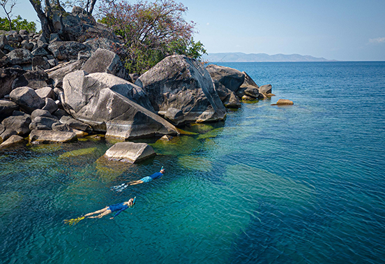 Two guests snorkeling among granite rocks and clear blue waters off Likoma Island, Lake Malawi.