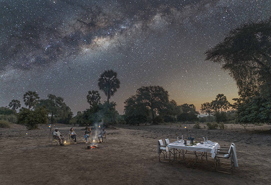 Guests dining under the Milky Way at a lantern-lit bush dinner arranged by Sausage Tree Camp in Lower Zambezi National Park.