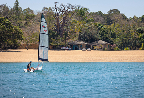 Guest sailing a small catamaran across the calm blue waters of Lake Malawi with Kaya Mawa in the distance.