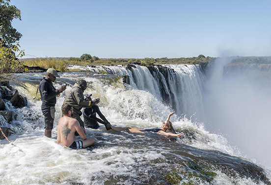 Visitors swimming in Devil’s Pool on the edge of Victoria Falls with a local guide, Livingstone, Zambia.