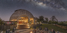 Milky Way above the domed main area of Ila Safari Lodge, illuminated by lantern light in Kafue National Park, Zambia.