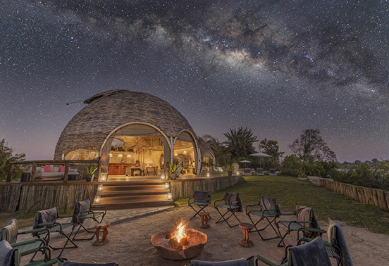 Milky Way above the domed main area of Ila Safari Lodge, illuminated by lantern light in Kafue National Park, Zambia.