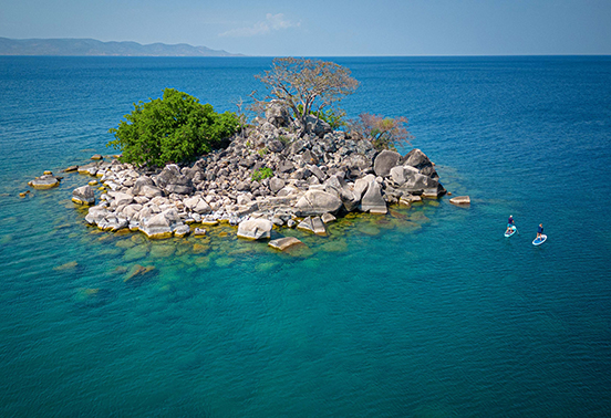 Guests paddleboarding around a rocky islet in the turquoise waters of Lake Malawi near Likoma Island.