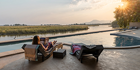 Guests relaxing beside the infinity pool with sunset views over the Zambezi River at Sausage Tree Camp, Zambia.