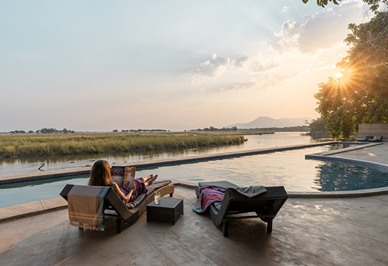 Guests relaxing beside the infinity pool with sunset views over the Zambezi River at Sausage Tree Camp, Zambia.
