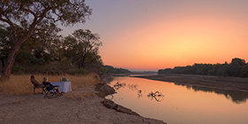 Guests enjoying sundowners along the Luangwa River at sunset near Shawa Luangwa Camp, Zambia.