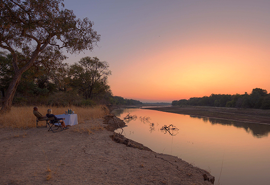 Guests enjoying sundowners along the Luangwa River at sunset near Shawa Luangwa Camp, Zambia.