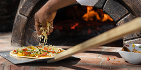 Chef preparing pizza with fresh toppings at the wood-fired oven at Tongabezi Lodge, Zambia.