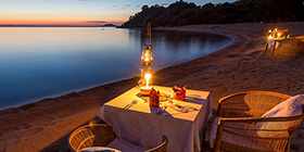 Romantic dinner set on the beach at Kaya Mawa, lit by lanterns under the Malawian night sky.