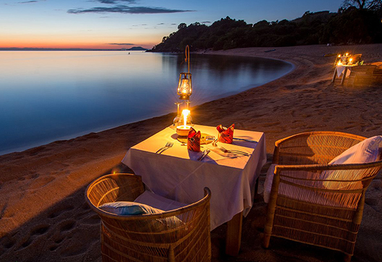 Romantic dinner set on the beach at Kaya Mawa, lit by lanterns under the Malawian night sky.