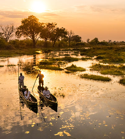 Guests traveling by mokoro canoe through shallow water at sunset in the Okavango Delta