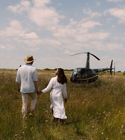 Couple walking through grass toward a helicopter in an open African landscape