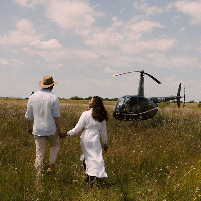 Couple walking through grass toward a helicopter in an open African landscape