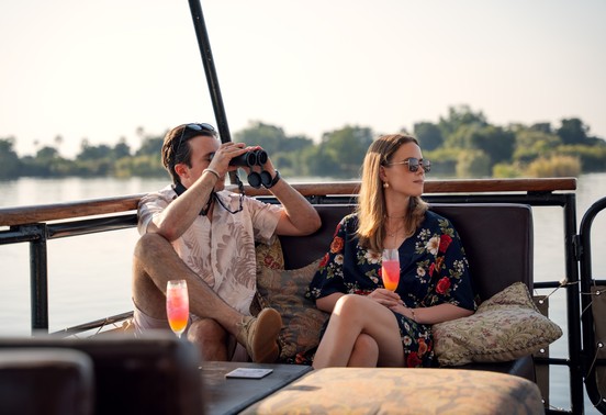 Couple with cocktails and binoculars enjoying a sunset cruise on the Zambezi River, Victoria Falls, Zimbabwe
