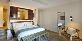 Spacious luxury suite interior with four-poster king bed, earthy tones, and open-plan bathroom at David Livingstone Safari Lodge, Zambia