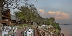 Candlelit outdoor dining deck set for dinner on the banks of the Zambezi River at David Livingstone Safari Lodge, Livingstone, Zambia