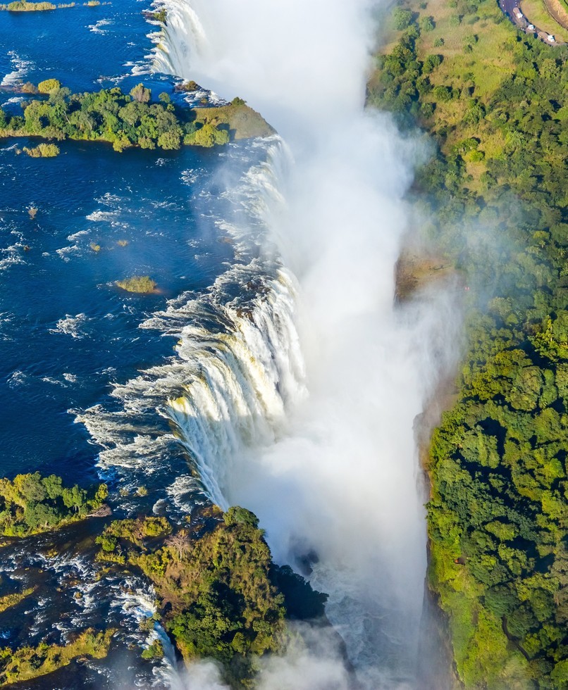 Aerial view of Victoria Falls with a vivid rainbow over the Zambezi River gorge and historic bridge, Zimbabwe
