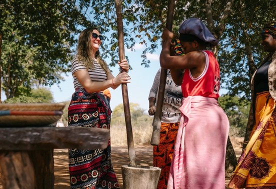 Guest laughing with local women while pounding grain during a village visit, Zimbabwe