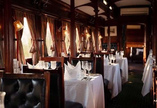 White-linen dining tables set for dinner inside a polished mahogany Bushtracks Express rail car, Victoria Falls, Zimbabwe
