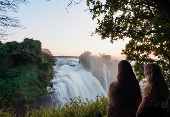 Two guests watching Victoria Falls in golden morning mist from the Zambian bank, Livingstone, Zambia