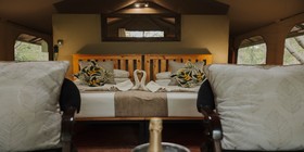 Elegant twin-bed interior with tropical cushions and towel swans at Iganyana Tented Camp, Zimbabwe