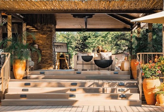 Raised outdoor lounge deck with terracotta pots and plush seating under a reed-and-timber pergola at Insinka Lodge, Victoria Falls, Zimbabwe
