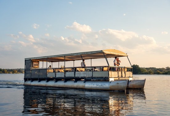 Bushtracks pontoon boat with guests cruising the Zambezi River at sunset, Victoria Falls, Zimbabwe