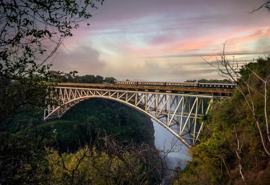 Royal Livingstone Express train crossing the historic Victoria Falls bridge at sunset, Livingstone, Zambia