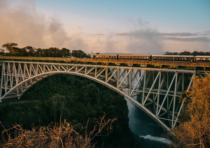 Royal Livingstone Express heritage train crossing the historic Victoria Falls Bridge at golden sunset, Zambia