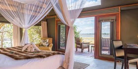 Four-poster canopied bed with Zambezi river views and private deck at Royal Zambezi Lodge, Lower Zambezi National Park, Zambia