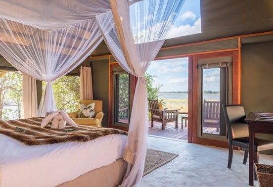 Four-poster canopied bed with Zambezi river views and private deck at Royal Zambezi Lodge, Lower Zambezi National Park, Zambia